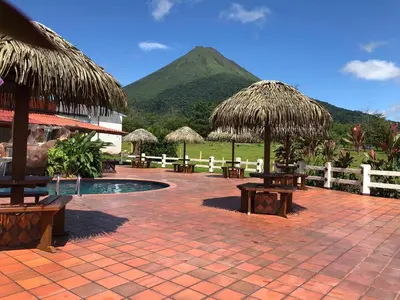 a patio with benches and umbrellas with a mountain in the background at Hotel La Pradera del Arenal in Fortuna