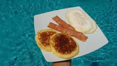 a plate of food with bacon and eggs and bread at Hotel La Pradera del Arenal in Fortuna