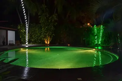 a swimming pool with green illumination at night at Café de Playa Beach Front Hotel in Coco