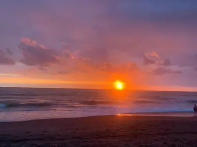 a sunset on the beach with a person walking on the beach at Hotel Mirasol in Jacó