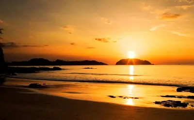 a sunset on the beach with a rock in the water at Casa del Sol -Villas Catalinas in Potrero
