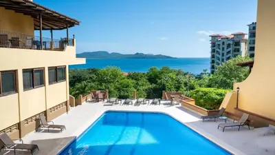 a swimming pool with chairs and a view of the ocean at Presidential Suites 15-Oceanview Condo in Playa Flamingo