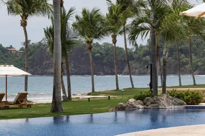 a swimming pool with palm trees and a beach at Palms 3- Luxury Beachfront Villa in Playa Flamingo