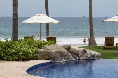 a swimming pool next to the beach with an umbrella at Palms 3- Luxury Beachfront Villa in Playa Flamingo