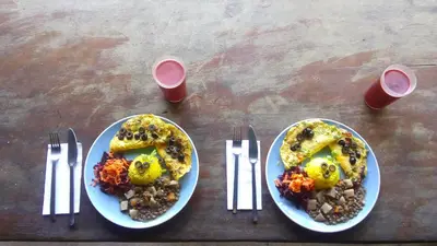 two plates of food on a wooden table with forks at Eco Lodge&Farm Rustic Roots Reserve in Drake