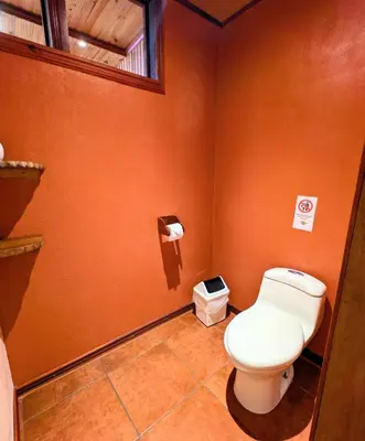 a bathroom with a toilet in an orange wall at Miztli Lodge & Adventure in Monteverde Costa Rica