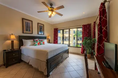 a bedroom with a bed with a ceiling fan and a television at Sunrise 38- Ocean View 2 Br Condo, Steps To The Beach in Tamarindo