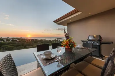 a dining table and chairs on a balcony with a sunset at Casa De La Perla, Ocean View 4 Bedroom Home in Tamarindo