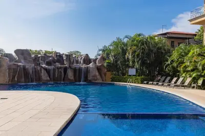 a swimming pool with a waterfall in a resort at Sunrise 6- Ocean View 2 Br Condo, Steps To The Beach in Tamarindo