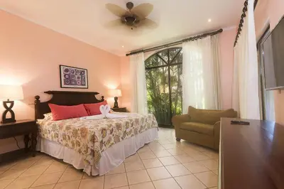 a bedroom with a bed with a fan and a chair at Sunrise 33- 3 Bedroom Poolside Condo in Tamarindo