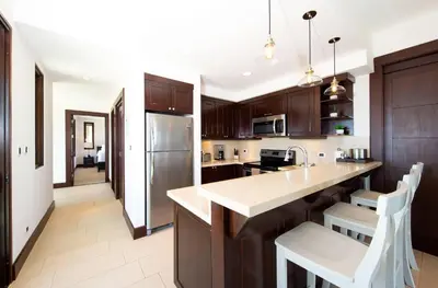 a kitchen with wooden cabinets and a kitchen island with white chairs at 360 Splendor 406-Ocean View Condo With Breakfast in Playa Flamingo