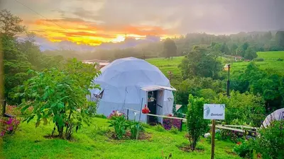 a tent in a field with a sunset in the background at Poas Volcano Observatory Lodge & Glamping in Poasito