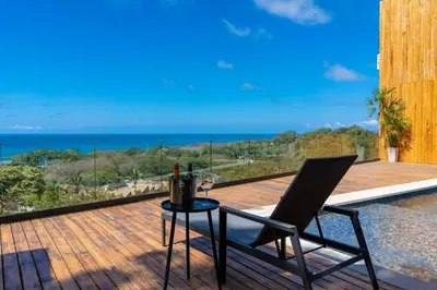a table and chair on a deck with a view of the ocean at Casa Olala Santa Teresa in Santa Teresa Beach