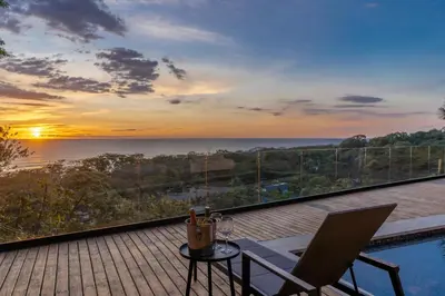 a balcony with a table and two chairs and the sunset at Casa Olala Santa Teresa in Santa Teresa Beach