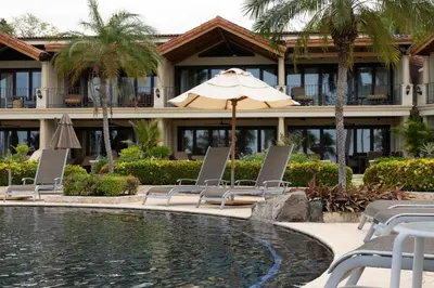 a hotel with chairs and an umbrella next to a pool at Palms 20 Luxury Oceanfront Villa in Playa Flamingo