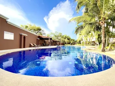 a large blue swimming pool with palm trees in front of a building at ✰Upscale 3Bdr condo✰ Incredible amenities ✰Fast wifi in Tamarindo