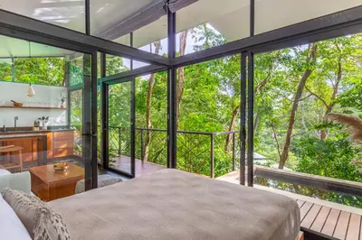 a bedroom with a bed and a balcony with trees at NAIA OCEANVIEW STUDIO in Carmen