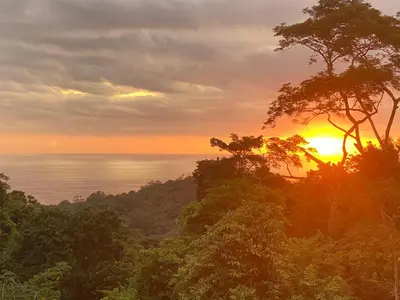 a sunset over the ocean with trees in the foreground at CASA BUHO and COZY JUNGLE CABANA in Santa Teresa Beach