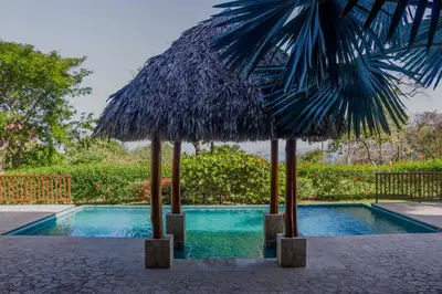 a swimming pool with two straw umbrellas next to it at Azul Paraíso 2B in Ocotal