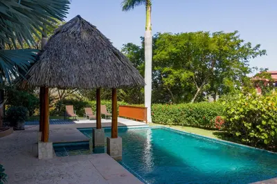 a swimming pool with a straw umbrella next to a resort at Azul Paraíso 2B in Ocotal