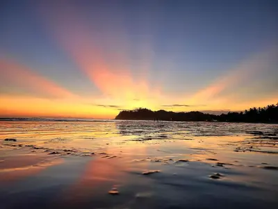 a sunset on the beach with a rainbow in the sky at Casa Terra Hostel in Sámara