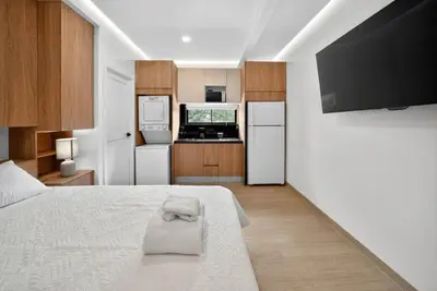 a bedroom with a white bed and a kitchen at Hotel Sabana Inn in San José