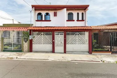 a white house with a red and white gate at Private bedroom 10 minutes from the SJO airport in Alajuela City
