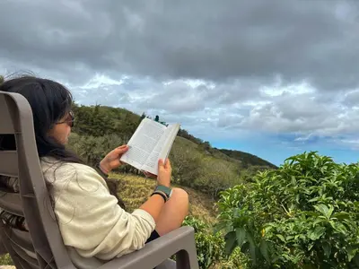 a woman sitting in a chair reading a book at Casa Urraca, Magnífica Vista al Océano Pacífico in Monteverde Costa Rica