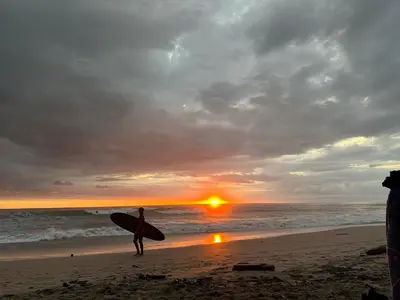 a person holding a surfboard on the beach at sunset at The Lizard in Santa Teresa Beach
