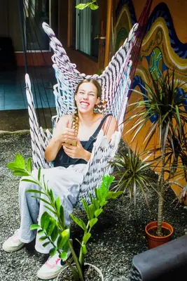 a woman sitting in a hammock holding a drink at Alpha Arenal Hostel in Fortuna