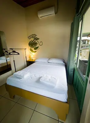 a bedroom with a bed with white sheets and a window at Alpha Arenal Hostel in Fortuna