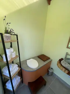 a bathroom with a toilet and a shelf with towels at Glamping Campo Alegre in Cartago
