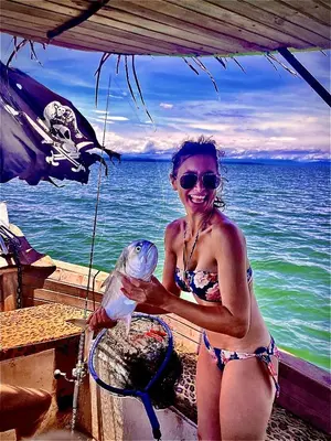 a woman in a bikini holding a fish on the beach at La Perla Negra Eco Pirate Resort in Puntarenas