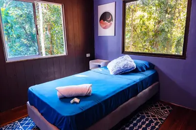 a bedroom with a bed with blue sheets and two windows at Miles Away in Cóbano