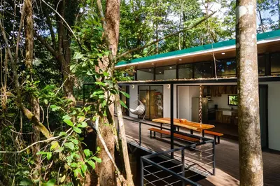 a house in the woods with a wooden table on a deck at Casa Henaway - Portasol Vacation in Savegre