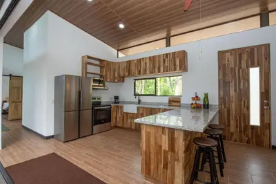 an open kitchen with wooden cabinets and a large island with bar stools at Casa Henaway - Portasol Vacation in Savegre