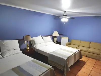 a blue room with two beds and a couch at Hotel Puerta del Sol - San Jose Airport in San José