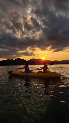 two people on a paddle board in the water at sunset at Bioluminiscencia Hostel Tours - South in Paquera