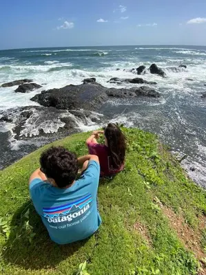 two people sitting on the grass looking at the ocean at Casa Bus los Guanacastes in Veintisiete de Abril