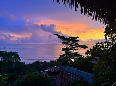 a sunset over the ocean with a house and trees at Villa Amor del Mar with Breathtaking View of Ocean & Jungle in Dominical