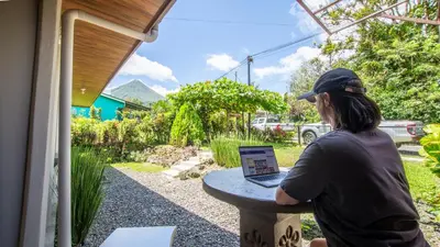 a person sitting at a table with a laptop at Arenal Dream Cottage in Fortuna