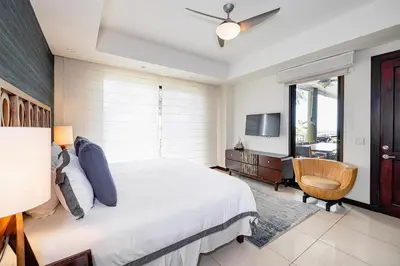a bedroom with a bed and a tv and a chair at Modern 3BR Condo with Partial Ocean View - Carao - Reserva Conchal Golf Resort in Playa Conchal