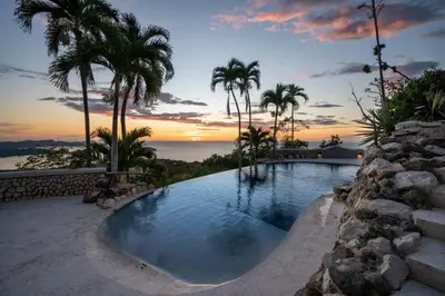 a swimming pool with palm trees and a sunset at Beautiful House with Sweeping Ocean Views, Modern Design, and a Private Infinity Pool in Potrero