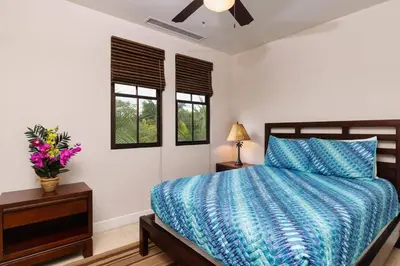 a bedroom with a bed with a blue comforter and two windows at 3-Bedroom 2-Bath Condo Overlooking Pool in Coco