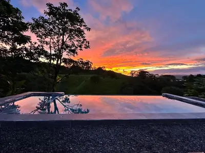 a sunset over a swimming pool at sunset at Chateau Arenal Hotel & Restaurante in El Castillo de La Fortuna