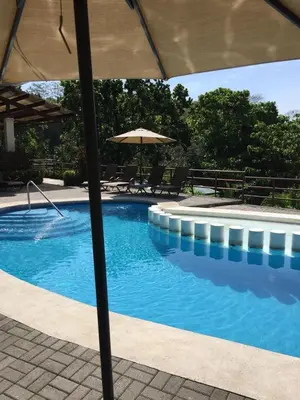 a large swimming pool with an umbrella and chairs at Casa de playa Herradura con piscina y jacuzzi in Puntarenas
