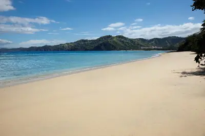 a beach with the ocean and mountains in the background at Riu Guanacaste - All Inclusive in Coco