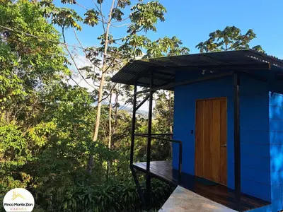 a blue house with a wooden door on a deck at Cabaña Montezion Bijagua in Bijagua